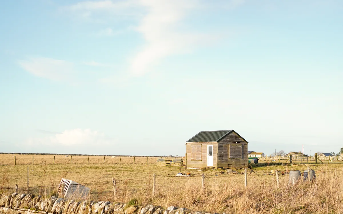 A small stone hut alone in a field of dry grass under a pale sky