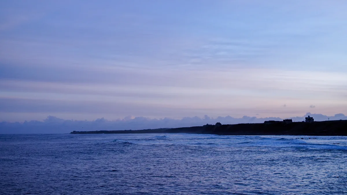 A blue dusk over the sea with a low headland on the horizon