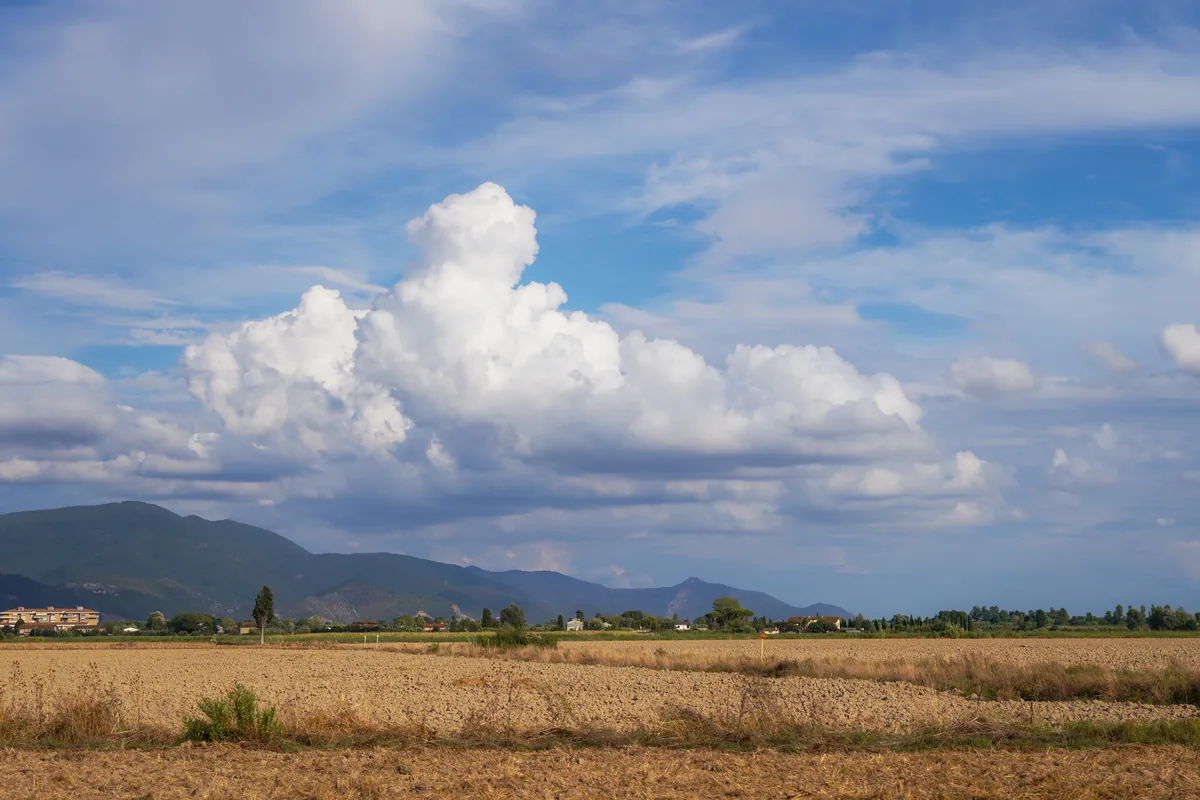 Towering white clouds over a harvested field and distant hills
