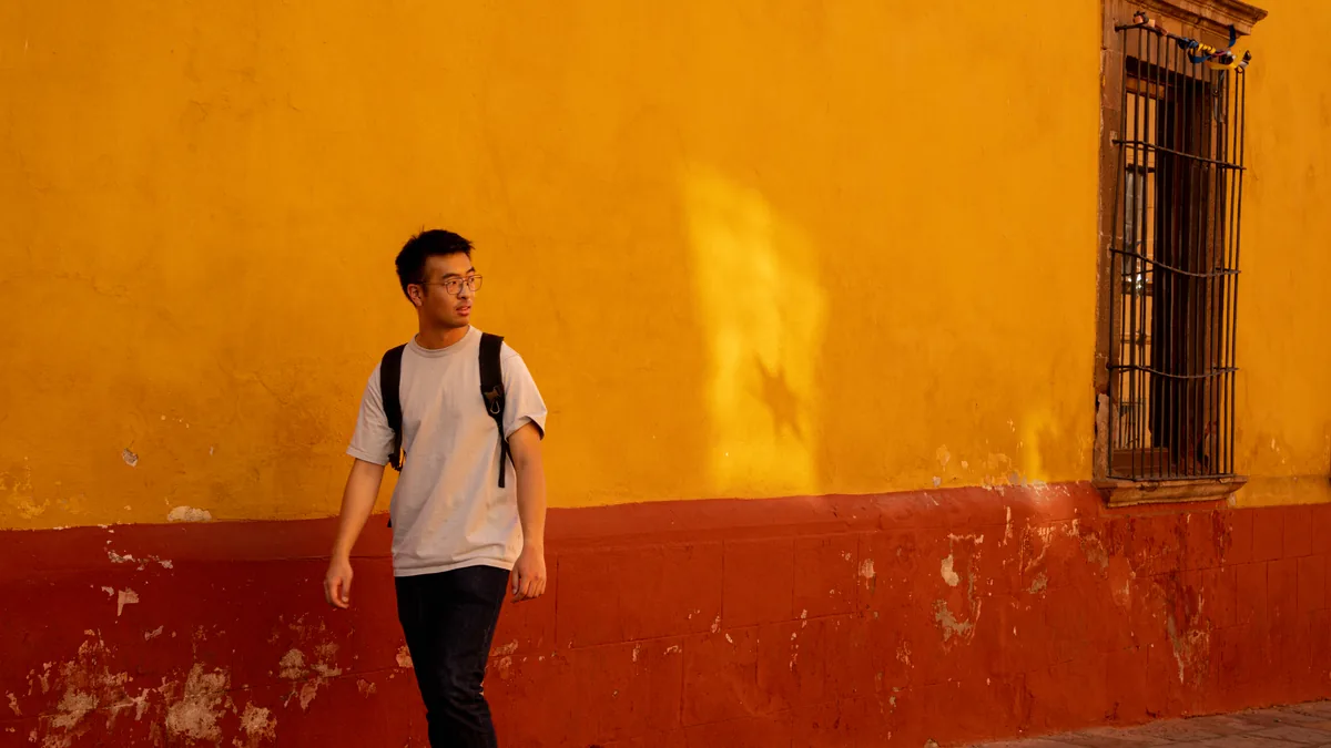A man with a backpack walking past a yellow and red wall