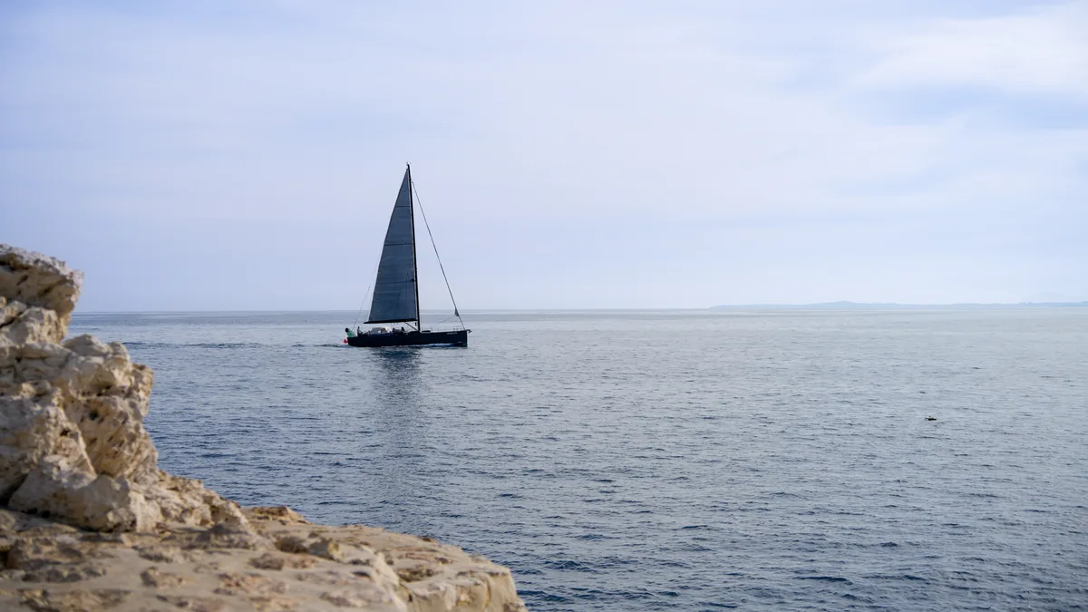 A sailing boat on a calm sea beside pale rocks