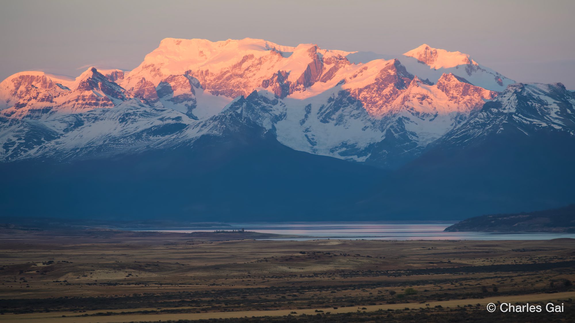 Snow peaks lit pink at dawn above a wide plain